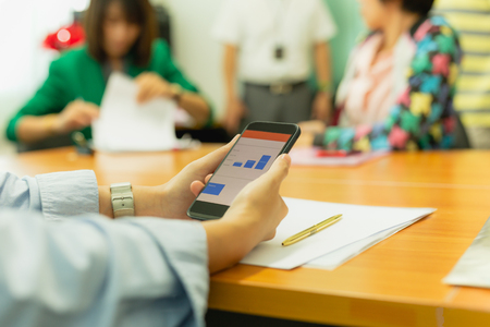 Hands using cell phone with stock money graph with group of business people.の写真素材