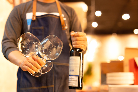 Glass of wing in waiter is hand with bottle red wine in background.の写真素材