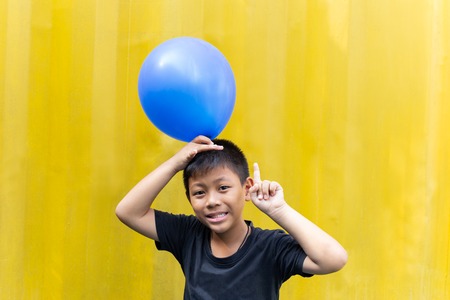 Boy holding blue balloons  standing on yellow