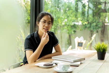 Asiam woman student eating cake with book and laptop in coffee shop.の写真素材