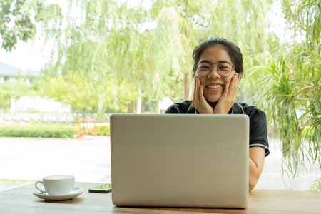 Asian woman student working on laptop with earphone looking at camera.の写真素材