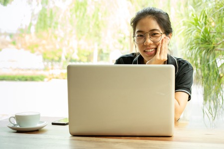 Asian woman student working on laptop with earphone looking at camera.の写真素材