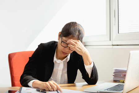 Businesswoman resting hands on head with eyes close at work desk in office.の写真素材