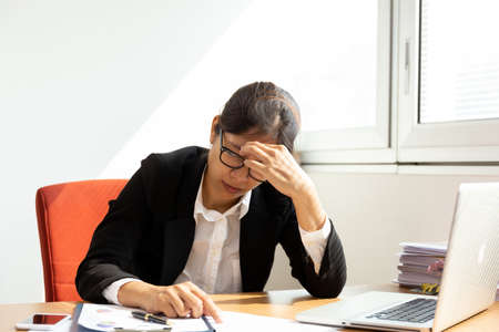 Businesswoman resting hands on head with eyes close at work desk in office.の写真素材