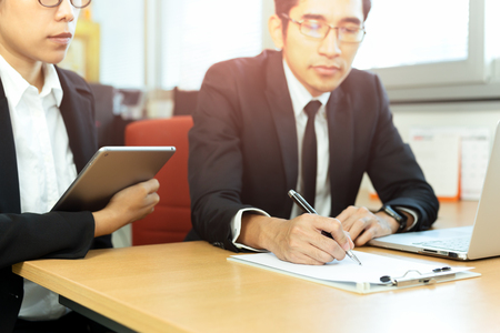 Business executive signing contracts with secretary at desk in office.の写真素材