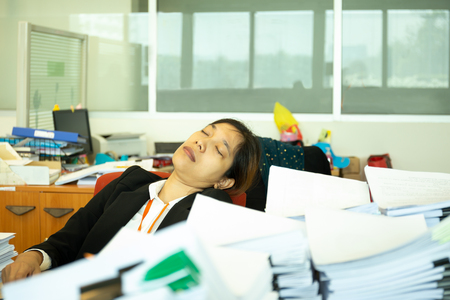 Exhausted Businesswoman sleeping on desk in office with pile of paperwok.の写真素材