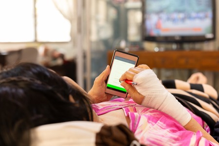 Senior patient hand injured with bandage lying down and using cell phone.の写真素材