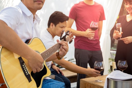 Group of friends having party with red wine and playing guitar outdoor.の写真素材