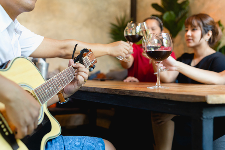 Group of friends celebrating and playing guitar while drinking red wine.の写真素材