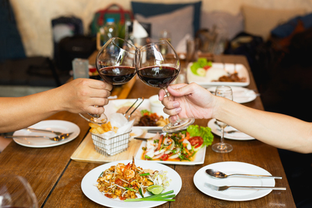 Friends celebration lunch with hands toasting glass red wine with food.の写真素材
