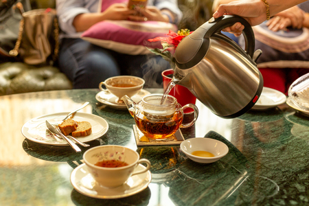 Waiter filling hot water into tea pot for customer with pice of cake on table.の写真素材