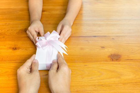 Two persons hands giving and receiving a present gift box on table.の写真素材