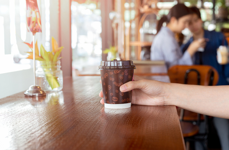 Woman hand holds out a paper cup of coffee to take away.の写真素材