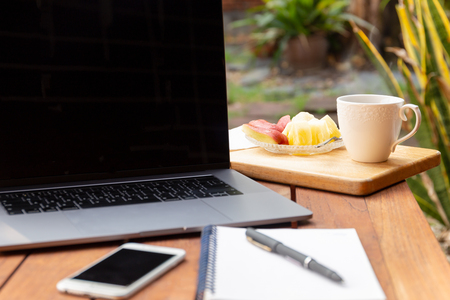 Coffee mug with fresh fruit and laptop on wooden table in the garden.の写真素材