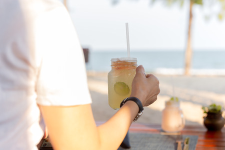 Woman relaxing on the beach with hand glass fresh lemon honey drink.の写真素材
