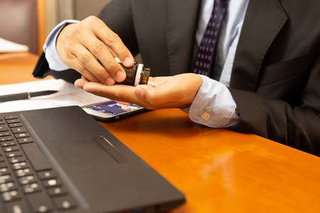Businessman taking painkiller pill with laptop on wooden table.の写真素材
