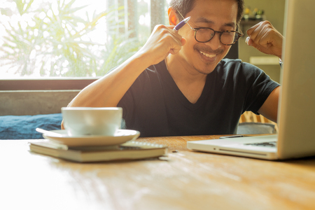 Asian man with laptop raised hands up celebrate success in great news.の写真素材