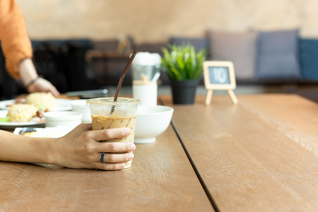 Holding glass of iced latte coffee with food on table at lunch time.の写真素材