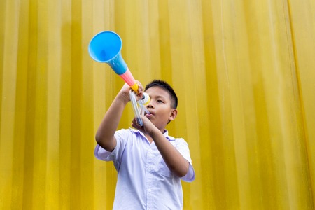 Asian school boy blowing a colorful horn in yellow background.の写真素材