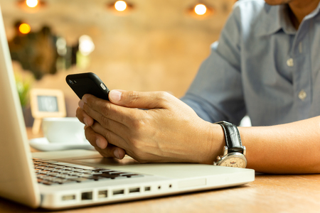 Businessman reading his smartphone while working on laptop.の写真素材