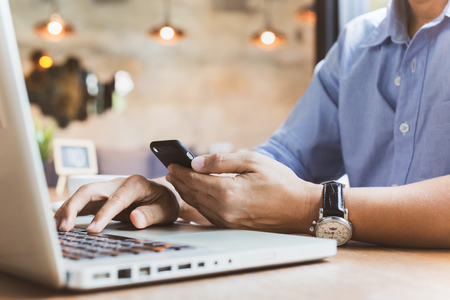 Businessman reading his smartphone while working on laptop.の写真素材