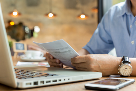 Businessman using laptop while looking at invoice.の写真素材