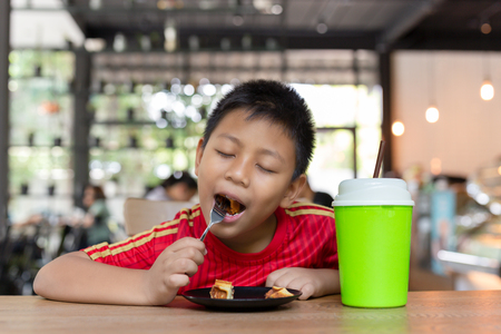 Happy face asian boy enjoy eating chocolate waffle in restaurant.の写真素材