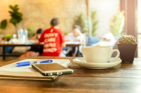 Cup of coffee with cell phone and book, pen on the table.の写真素材
