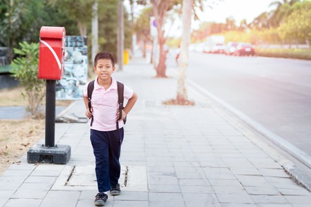 Asian school boy in uniform with backpack walking back home.の写真素材