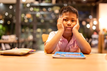 Asian school boy hand on his face dressed while doing his home work.の写真素材