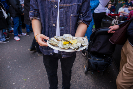 Man hand holding fresh raw oyster in paperr plate with lemon in market.の写真素材