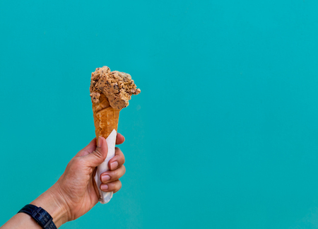 Female hand holding ice cream cone isolated on blue pastelの写真素材