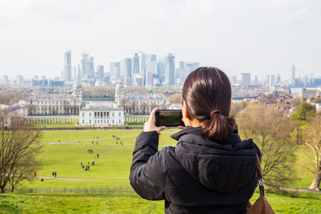 Woman tourist taking pictures in the park with city buildingの写真素材