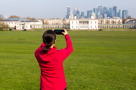 Woman tourist taking pictures of building in the park with cell phone.の写真素材