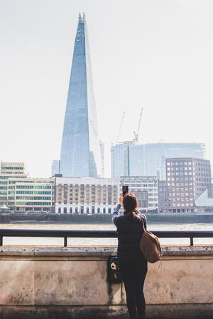 Tourist woman taking picture of building and river Thames with cell phone.の写真素材