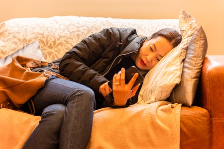 Beautiful woman relaxed using smart phone lying on a sofa in the living room.の写真素材