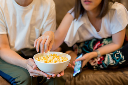 Woman hands taking popcorn from bowl watching movie with friend.の写真素材