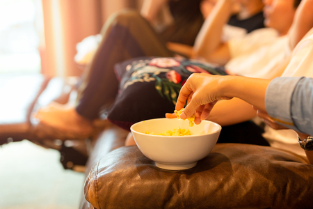 Hands taking popcorn from bowl watching movie with friends.の写真素材