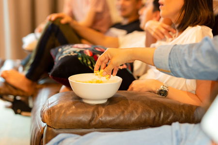 Woman hands taking popcorn from bowl watching movie with friend.の写真素材