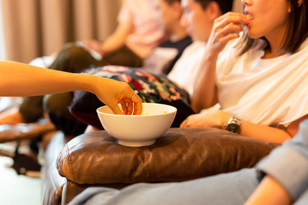 Woman hands taking popcorn from bowl watching movie with friend.の写真素材