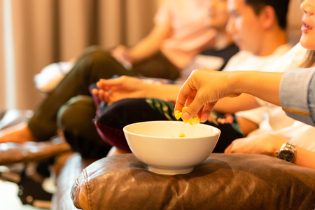 Woman hands taking popcorn from bowl watching movie with friendの写真素材