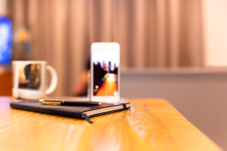Notebook and pen with cell phone on wooden table in hotel room.の写真素材