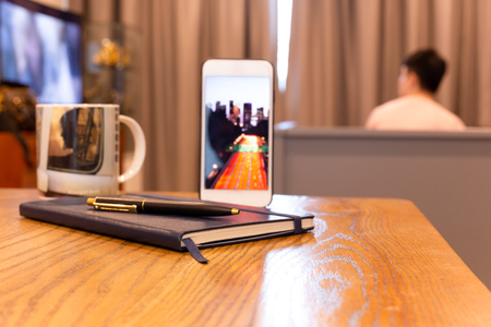 Notebook and pen with cell phone on wooden table in hotel room.の写真素材