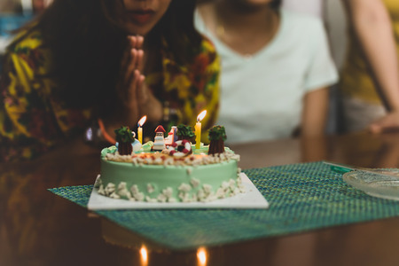 Shot in low light woman blowing on candles on birthday cake with friends.の写真素材