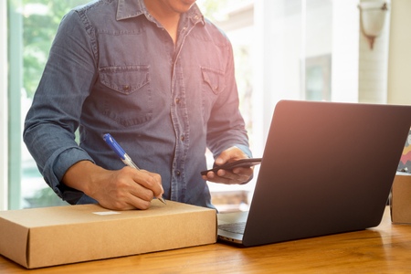 SME Business man looking cell phone and writing address on parcel.の写真素材
