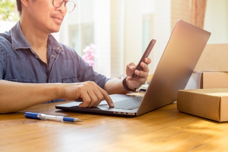 SME Businessman looking at cell phone and work on laptop with parcel on table.の写真素材