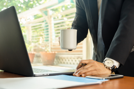 Businessman holding coffee mug  with laptop on table.の写真素材
