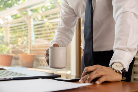 Businessman holding coffee mug  with laptop on table.の写真素材