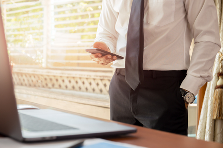 Businessman looking at cell phone with laptop on wooden desk.の写真素材