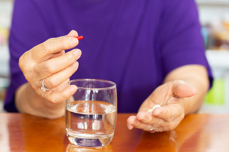 Senior woman hands holding tablet with glass of water on table.の写真素材